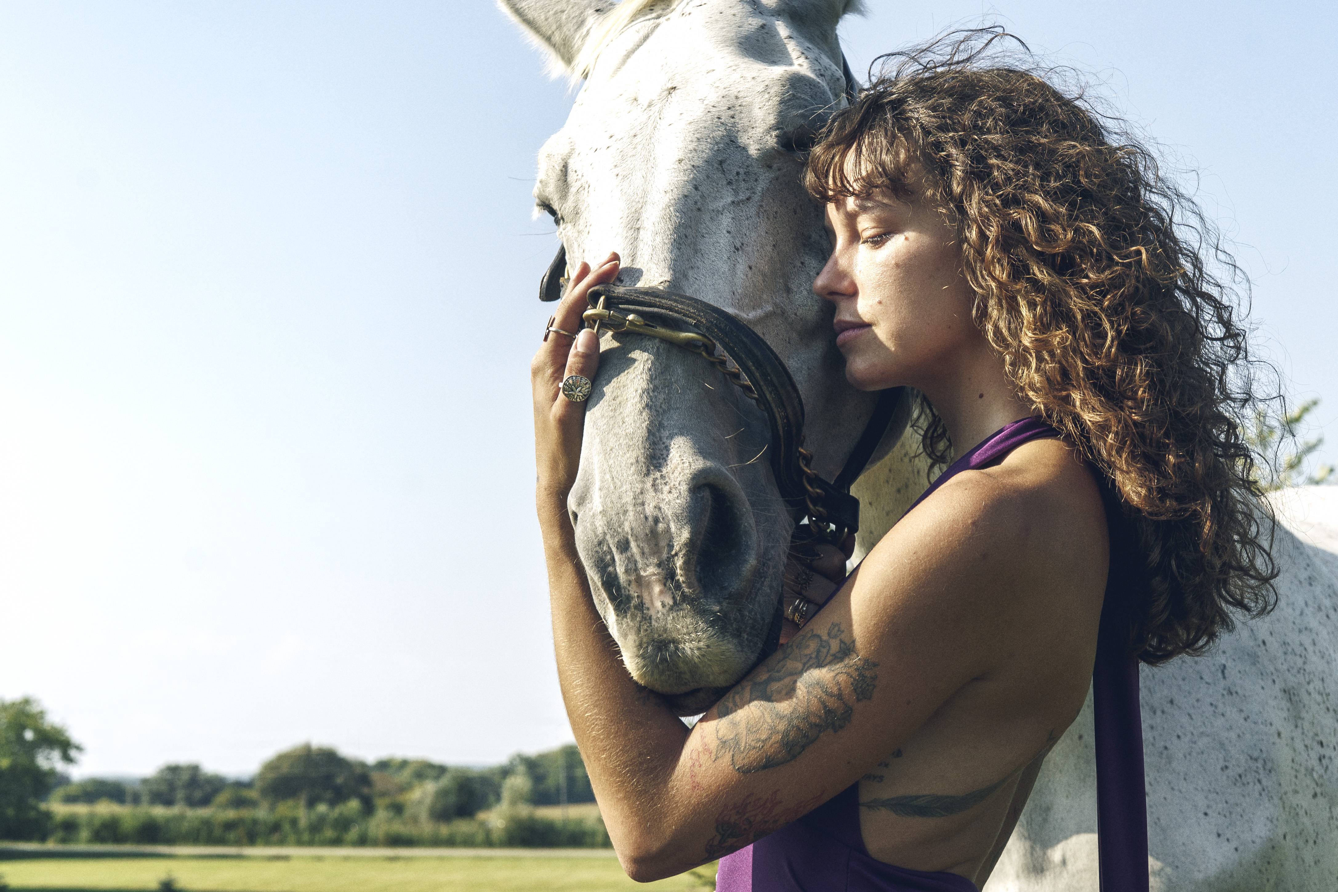 editorial fashion photography — woman with curly hair embracing white horse, intimate equestrian lifestyle campaign, Born to Be Free, by Daniyar Sadykov